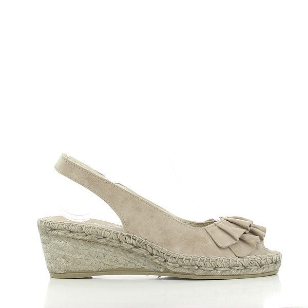 The Calzanor 1536 Volantes Taupe Slingback Espadrilles are elegantly displayed on a rustic wooden surface. The espadrilles feature a soft taupe leather upper adorned with delicate ruffles along the strap, adding a touch of femininity. The round toe shape gives them a classic look, while the 6 cm heel provides a subtle lift. The jute-wrapped sole highlights the traditional craftsmanship and sustainable materials used in their construction.
