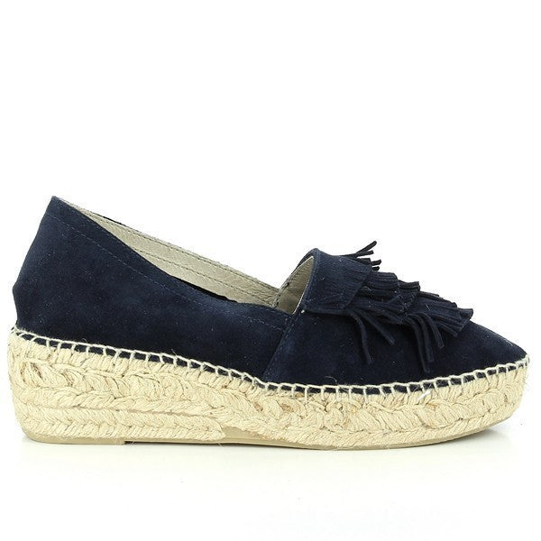A pair of Calzanor 2045 Navy Fringe Espadrilles sits elegantly on a textured surface, showcasing their handcrafted beauty. The deep navy leather upper is adorned with delicate fringe detailing, adding a touch of playful sophistication. The espadrilles feature a round toe and a comfortable 5 cm heel-platform, perfectly balanced for style and support. The natural jute sole peeks out from beneath, highlighting the eco-friendly craftsmanship and sustainable materials used in their creation.