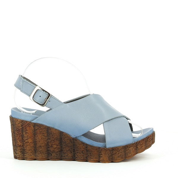 A side profile showcasing the light blue leather upper, cork wedge sole, and the sleek cross-strap design with the slingback strap resting elegantly on the ankle.