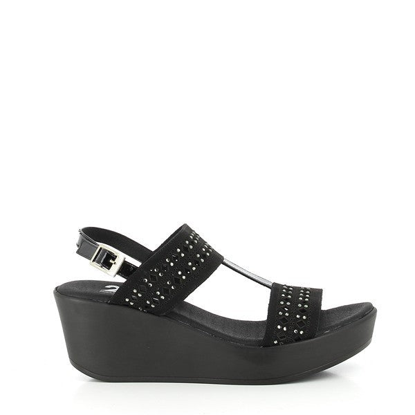 A pair of 24 Hrs 24053 Black Slingback Wedges is displayed on a neutral backdrop. The wedges feature a classic black leather upper with a sleek round toe and an adjustable buckle fastening at the ankle. The 5.5 cm wedge heel adds a subtle lift while maintaining stability. The leather lining is visible from the top, highlighting the attention to detail and comfort. The overall design combines sophistication with functionality, making these wedges a versatile choice for various occasions.