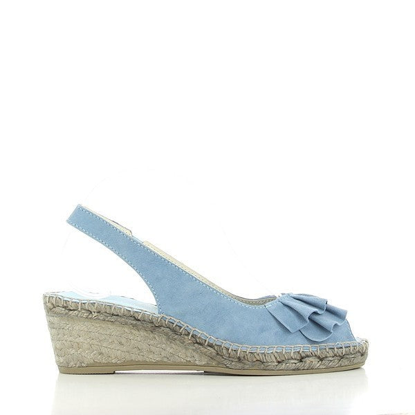 The photo showcases a pair of Calzanor 1536 Volantes Light Blue Slingback Espadrilles elegantly positioned on a textured surface. The espadrilles feature a light blue leather upper with delicate ruffle detailing along the straps, adding a touch of femininity. The round toe design and a modest 6 cm heel provide a stylish yet comfortable look. The natural jute sole is visible, emphasizing the eco-friendly craftsmanship. 