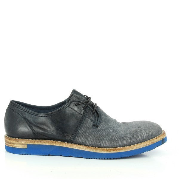 A close-up of the shoe's side profile, showcasing the elegant black and grey leather upper. The smooth texture and hand-buffered finish highlight the craftsmanship, with the bold blue sole adding a striking contrast.